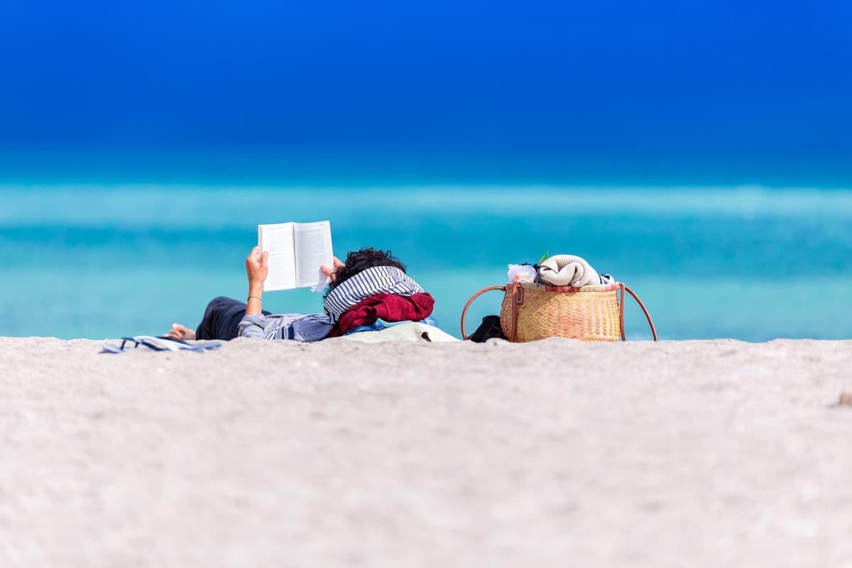 Person relaxing on beach reading book