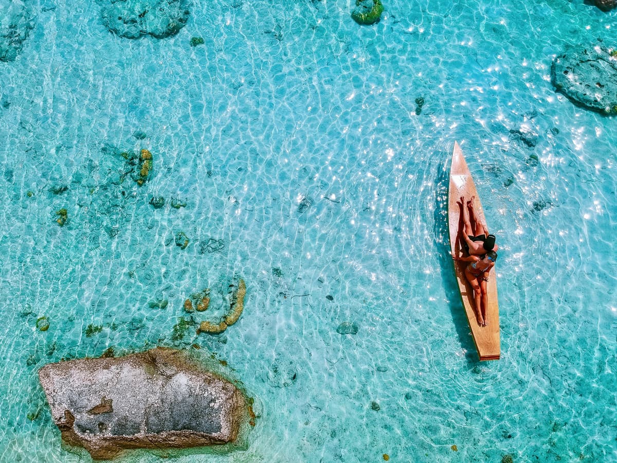 Birds-eye-view of couple seated on surf board in clear sea water on sunny day